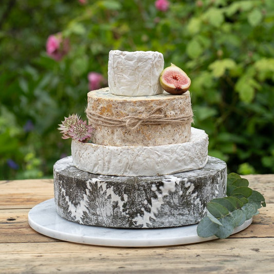 Four-tier celebration cheese cake decorated with fig, flowers and greenery