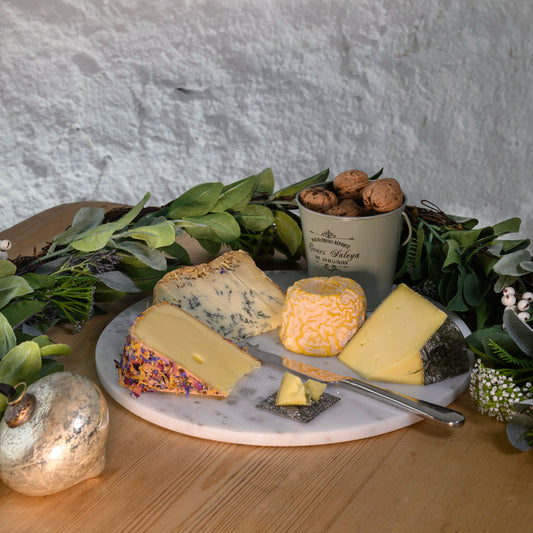 Assorted cheeses on a marble board with a mug of wine and decorative elements.